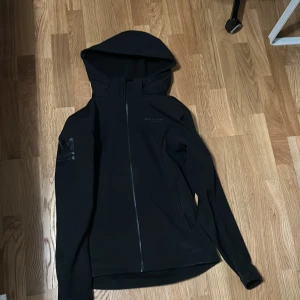 Svart vindjacka från Race Marine S - Svart vindjacka från Race Marine med hel dragkedja och huva. Jackan har stilren design med diskret logga på bröstet och är tillverkad i ett slätt syntetmaterial. Perfekt för dig som gillar sportig och clean look.