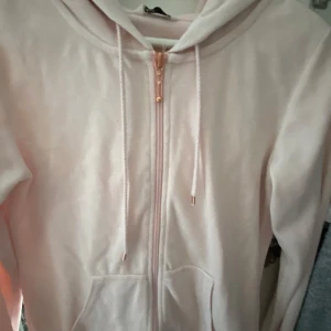 Ljusrosa hoodie med dragkedja - Mysig ljusrosa hoodie med huva och dragkedja framtill. Tröjan har fickor på magen och snörning i huvan. Perfekt för chill dagar eller när du vill vara extra bekväm.