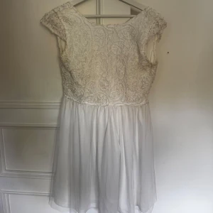 Vit spetsklänning med knappar - Superfin vit kortklänning med spets upptill och lätt, flowy kjol. Klänningen har korta ärmar, v-ringning i ryggen och dekorativa knappar bak. Perfekt för dig som gillar romantisk och söt stil. Kan mötas upp i Norrköping😊