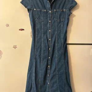 Jeansklänning från Creeks Denim , storlek 16,XS - Snygg jeansklänning från Creeks Denim med korta ärmar, knappar hela vägen framtill och två bröstfickor. Klänningen har klassisk skjortkrage och är figursydd för en cool och avslappnad look. Perfekt för dig som gillar denim och vill ha något unikt i garderoben.