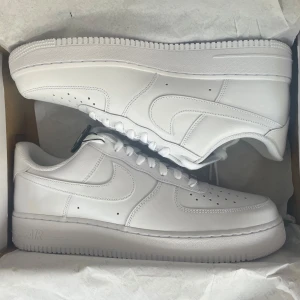 Nike Air Force 1 '07 helvita sneakers - Nypris 1399kr!!! Klassiska Nike Air Force 1 '07 i helvitt skinn med perforerad tå, vit sula och snörning. Snygg och tidlös modell som passar till allt, med låg profil och ikonisk Swoosh på sidan. Perfekta för dig som gillar cleana och fräscha sneakers.