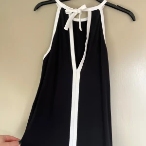 Chic topp med knytning - Snygg svart ärmlös topp med vit kant och knytning. Bra passform men lite för liten för mig med större byst. 