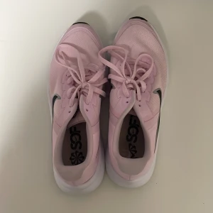 Rosa Nike sneakers - Säljer ett par rosa Nike sneakers med vit sula och svart Nike-logga. Skorna har snörning och en sportig design, perfekt för träning eller vardagsbruk.