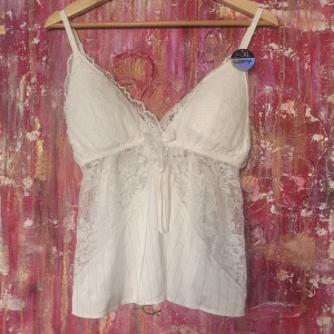 Vit spetsblus med knytband - Säljer en romantisk vit blus med spetsdetaljer och knytband framtill. Blusen har en luftig passform och är perfekt för varma dagar. Den är ärmlös och har en vacker spetsdesign som ger en feminin touch. Har lappar kvar så är i nyskick 🩷 säljer en likadan i svart🩷