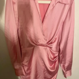 Rosa festklänning 🩷 - Säljer en snygg rosa omlottklänning från Zara i satin. Klänningen har långa ärmar och en v-ringad design med knappar vid ärmsluten och dragkedja på sidan.🩷 aldrig använd endast testad, köpt av en annan här på Plick 🩷🩷