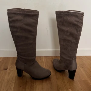 Bruna stövlar med klack - Snygga bruna stövlar i mocka med hög klack och dragkedja på insidan. Perfekta för höst och vinter med en stilren design som passar till många outfits.