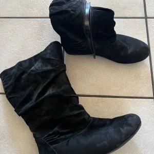 Svarta mockastövlar med dragkedja - Snygga svarta stövlar i mocka med dragkedja på sidan. Perfekta för höst och vinter med en stilren design och låg klack. Passar bra till både jeans och klänning.