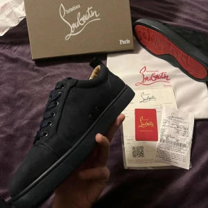 Svarta sneakers från Christian Louboutin - HAR MÅNGA FLER I OLIKA FÄRGER OCH STORLEKAR DM VIA INTRESSESnygga svarta sneakers från Christian Louboutin med den ikoniska röda sulan. Skorna har en stilren design med snörning och är tillverkade i ett elegant material. Perfekta för att ge din outfit en lyxig touch. 