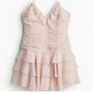 Ljusrosa klänning med volanger - Söt ljusrosa klänning med smala axelband och volanger. Den har en v-ringad design och flera lager av volanger. Aldrig använd, lappen sitter kvar! 