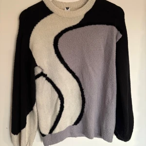  stickad tröja - Säljer en unik stickad tröja med abstrakt mönster i svart, vit och grå. Tröjan har långa ärmar och en rund halsringning. Perfekt för att hålla sig varm och stilren under kyliga dagar.