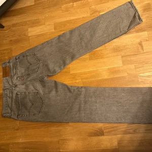 Grå jeansbyxor från Levis - Snygga grå jeansbyxor från Levis med klassisk femficksdesign och en rak passform. Perfekta för en avslappnad stil. De har en midwaist och är tillverkade i slitstarkt denim. 