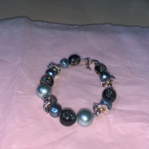Färgglatt armband med pärlor - Unikt armband med en mix av färgglada pärlor och metalliska detaljer. Pärlorna har olika färger och mönster, vilket ger ett livfullt och lekfullt intryck. Perfekt för att lägga till en färgklick till din outfit.