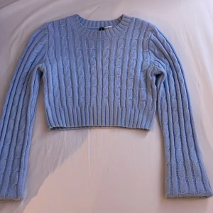 Ljusblå stickad croppad tröja från H&M - Säljer en ljusblå stickad croppad tröja från H&M. Tröjan har ett snyggt kabelstickat mönster och långa ärmar. Perfekt för en stilren och trendig look. Passar bra till både jeans och kjol.