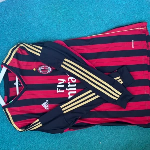 AC Milan fotbollströja med Maldini 3 - Säljer en klassisk AC Milan fotbollströja från Adidas med Maldini och nummer 3 på ryggen. Tröjan är randig i rött och svart med guldiga detaljer på ärmarna. Perfekt för fans av den legendariska spelaren!