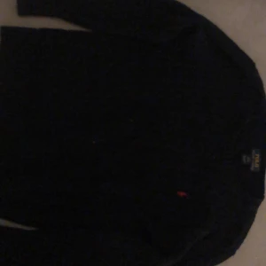 Mörkblå tröja från Ralph Lauren - Säljer en stilren mörkblå tröja från Ralph Lauren med en liten röd logga på bröstet. Tröjan har långa ärmar och är perfekt för en klassisk look. Passar bra till både jeans och chinos.