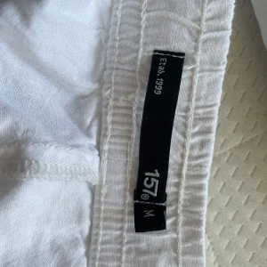 Vita linnebyxor från 157 - Säljer ett par vita linnebyxor från 157. Byxorna har en avslappnad passform med elastisk midja och dragsko för extra komfort. Perfekta för varma dagar med sin lätta och luftiga känsla.