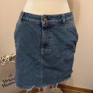 Jeanskjol  - Snygg jeanskjol med rå kant och klassisk femficksdesign. Kjolen har en knapp och dragkedja framtill. Perfekt för en avslappnad stil.
