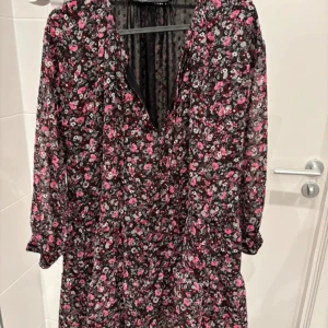 Blommig klänning Zara - Säljer en söt blommig klänning i svart och rosa med v-ringning och knytband framtill. Klänningen har långa ärmar med knappar vid ärmsluten. Perfekt för en romantisk look! Med prislapp 