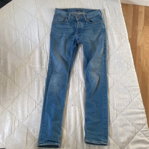 Blå jeans från Nudie Jeans - Snygga blå jeans från Nudie Jeans med klassisk femficksdesign och en bekväm passform. De har en tydlig logga på bakfickan och är perfekta för en avslappnad stil. Passar bra till både sneakers och kängor.