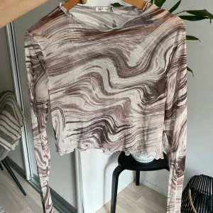 Mönstrad långärmad topp från Neyone - Säljer en unik långärmad topp från Neyone med ett abstrakt mönster i bruna och vita nyanser. Toppen är croppad och har en luftig passform, perfekt för en trendig look.