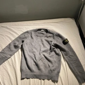 Grå stickad stone island tröja - Grå stone island tröja i storlek 140 men har krympt lite så den är ungefär i storlek 130. Den enda defekten är ett litet hål på högra armen. Annars är den som ny