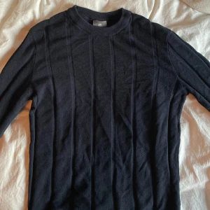 Marinblå tröja från H&M - Säljer en stilren marinblå tröja från H&M i slim fit. Tröjan har ett diskret mönster och långa ärmar, perfekt för en elegant look. Passar bra till både vardag och mer uppklädda tillfällen. Använd 1-2 gånger samt tvättad 1-2