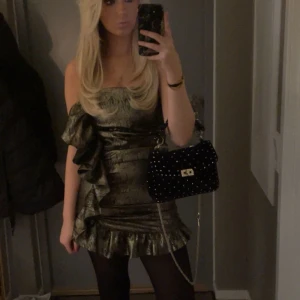 Guldig axelbandslös klänning från zara - Snygg guldig klänning i mörk ton med volangdetaljer. Den är axelbandslös och kort, perfekt för en utekväll. Klänningen har en figurnära passform som framhäver silhuetten. Storlek m men passar oss som är s men är lite längre eftersom zaras klänningar ofta är väldigt korta på mig som är 173. Använd en gång och bandet är avklippta