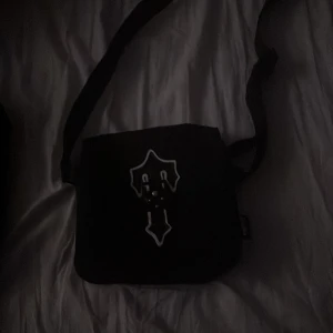 Svart axelväska från Trapstar - Snygg svart axelväska från Trapstar med ett unikt spänne framtill. Väskan har en justerbar axelrem och flera fack med dragkedja för praktisk förvaring. Perfekt för att bära med sig det nödvändigaste med stil. 9/10 skick äkta använd runt 10-15 gånger