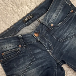Blå jeans från ONLY - Snygga blå jeans från ONLY med en klassisk femficksdesign och knappgylf. De har en lätt tvättad look som ger en avslappnad stil. Perfekta för en casual outfit.