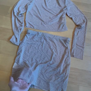 Beige glittrig set - Snygg beige kjol med glittriga detaljer. Perfekt för att sticka ut med sin skimrande look. Matcha med en topp för en komplett outfit. Najs att ha över bikini på stranden