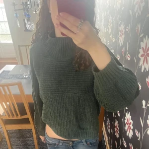 Mörkgrön stickad tröja - Säljer en mysig mörkgrön stickad tröja med hög krage och långa ärmar. Perfekt för kyliga dagar. Tröjan har en avslappnad passform och ribbade detaljer vid ärmslut och nederkant. Nopprig så därav det låga priset💛💛