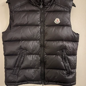 Svart dunväst från Moncler - Snygg svart dunväst från Moncler dragkedjan är sönder vid fickan.