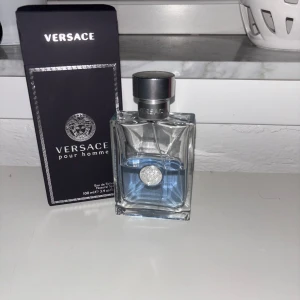 Versace Pour Homme Eau de Toilette - Säljer en elegant Versace Pour Homme Eau de Toilette i en stilren glasflaska med silverfärgad kork. Doften är fräsch och maskulin, perfekt för den moderna mannen. Flaskan rymmer 100 ml och kommer i en snygg svart kartong med Versace-logotypen.