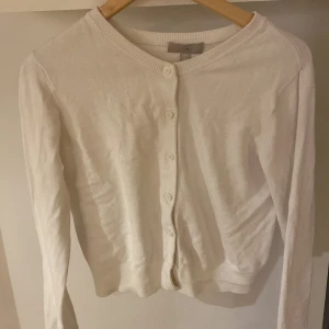 Vit kofta - Säljer en klassisk vit kofta med rund halsringning och knappar framtill. Perfekt för lager-på-lager och passar till många olika outfits. Koftan har långa ärmar och är i ett mjukt material.💖