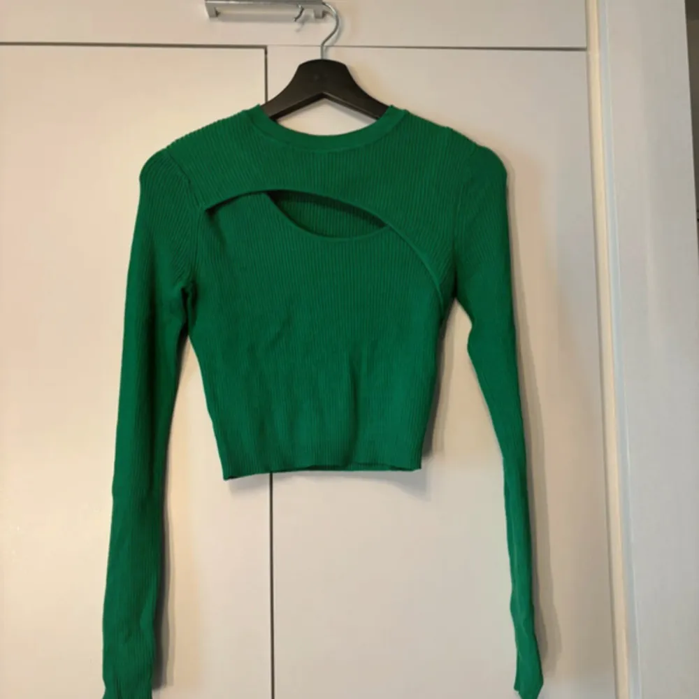 Snygg grön ribbad tröja med en unik cut-out detalj vid halsen. Tröjan har långa ärmar och en croppad passform, perfekt för en trendig look. Passar utmärkt till både jeans och kjol.. Neuletakit & Villapaidat.