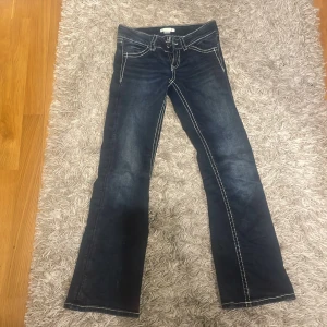 Mörkblå jeans med broderade fickor - Snygga mörkblå jeans med kontrastsömmar och unika broderade detaljer på bakfickorna. Byxorna har en klassisk femficksdesign och en bootcut-stil som ger en avslappnad look. Perfekta för dig som vill ha något extra i garderoben!