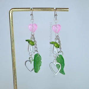 Söta örhängen med hjärtan och blad - Silvret är ej äkta och kan innehålla nickel. Detaljerna på örhängena innehåller både akrylpärlor och glaspärlor. Örhängen är designade med rosa hjärtan, gröna blad och silverfärgade hjärtan.