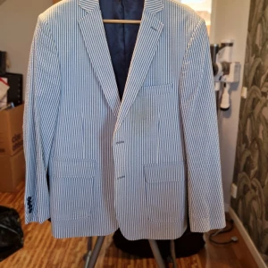 Randig kavaj i blått och vitt - Snygg randig kavaj i blått och vitt med två knappar framtill. Perfekt för en stilren look. Kavajen har klassiska slag och fickor fram.