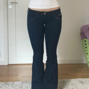 Mörkblå bootcut jeans från Hollister - Snygga mörkblå bootcut jeans från Hollister med klassiska femficksdesign och kontrastsömmar. Perfekta för en avslappnad stil med en touch av retro. De har en lågmidjad passform som ger en bekväm känsla.