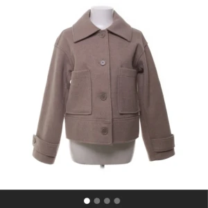 kappa från Kappahl - Snygg beige kappa med stora knappar och bred krage. Jackan har långa ärmar med dekorativa knappar vid ärmsluten och två stora fickor framtill. Perfekt som jacka till våren. 