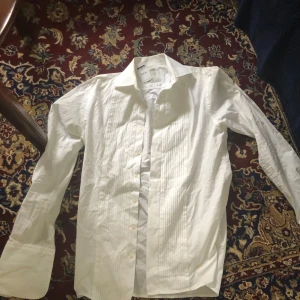 Vit skjorta  - Snygg vit skjorta köpt från Emmaus i stockholm med klassisk krage och knappar framtill. Skjortan har ett diskret randigt mönster och är perfekt för en stilren look. Tillverkad i bomull för en bekväm känsla. Endast testad ej använd, sitter som s/m