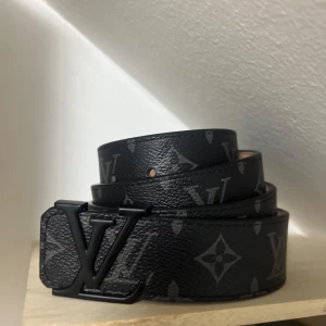 LV bälte svart  - Snyggt svart bälte från Louis Vuitton med det klassiska LV-mönstret. Bältet har en stilren svart spänne med LV-logotypen. Tillverkat i Frankrike och perfekt för att ge en lyxig touch till din outfit. Bältet är 115cm lång, vid frågor eller funderingar hör av er!