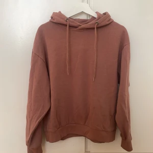 Dammrosa/rostfärgad hoodie  - Säljer en snygg rosa rostfärgad hoodie från 157. Den har en klassisk design med huva och dragsnören. Perfekt för en avslappnad stil. Passar bra till jeans eller mjukisbyxor. 