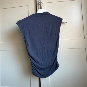 Mörkblå/grå ärmlös topp - Säljer en stilren grå/blå ärmlös topp i mjukt material. Perfekt för varma dagar eller som ett lager under en jacka. Toppen har en enkel design med en rund halsringning.