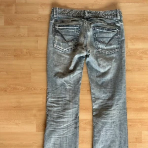 Blå jeans med nitar och strassdetaljer - Snygga ljusblå jeans från Miss Sixty med coola nitar på linningen och strassdetaljer på bakfickorna. Modellen har låg midja och utsvängda ben, klassisk femficksdesign och slitningar för en trendig look.