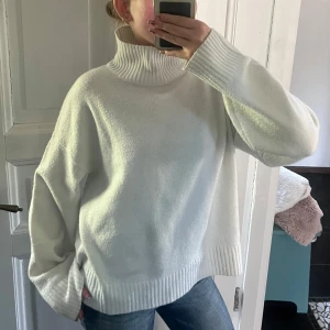 Stickad polotröja  - Säljer en vit polotröja med bred, ribbad krage och muddar. Tröjan har en loose passform och långa ärmar, perfekt för att hålla sig varm. Materialet är mjukt och stickat, vilket gör den supermysig att bära. Enkel och clean look som funkar till jeans eller andra favoritplagg.