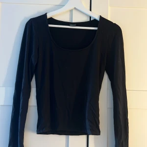 Svart långärmad topp med slits - En svart långärmad topp från Gina tricot med rundad, djup urringning och slitsdetalj vid ärmslut. Enkel och stilren design som passar perfekt till jeans eller kjol. Mjuk och stretchig bomullskvalitet för en bekväm känsla.