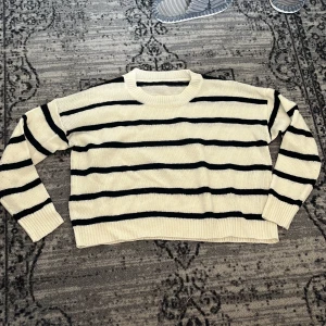 Randig stickad tröja i vitt och svart - Säljer en randig svartvit stickad tröja. Tröjan har rund hals, långa ärmar och ribbade muddar vid ärmslut och nederkant. 
