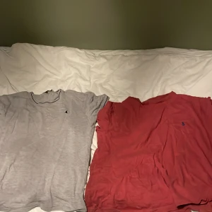 Grå och röd t-shirt från Polo Ralph Lauren - Två stilrena t-shirts från Polo Ralph Lauren i storlek XL. Ena är grå med svart broderad logga och smal passform, den andra är röd med blå broderad logga. Båda har rund hals och korta ärmar, tillverkade i mjuk bomull. Perfekt för en chill och snygg look.