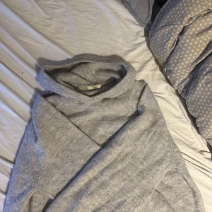 Grå stickad hoodie från Gina  - Mysig grå hoodie från gina med huva och långa ärmar. Stickad i mjukt material som känns skönt mot huden. Perfekt för chill dagar och när du vill ha en enkel, clean look. Ribbad kant vid ärmslut och nederkant för extra comfort.